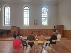Menschen auf Stühlen in einem Bethaus im Halbkreis vor einer Kerze