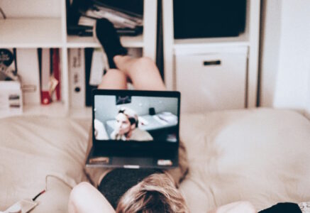 Eine Frau liegt auf einem Sofa und schaut einen Film auf ihrem Laptop auf dem Bauch.