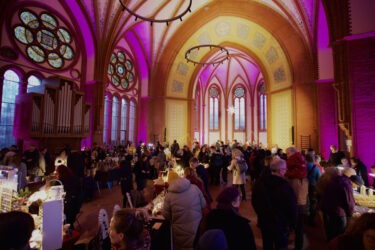 Adventsmarkt im gelb-rosa beleuchteten Kirchenraum der Heilandskirche Leipzig