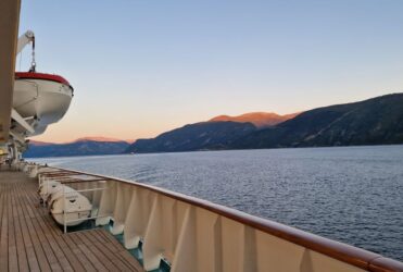 Reeling eines Kreuzfahrtschiffes auf dem Meer mit Sonnenaufgang an einem Berg im Hintergrund